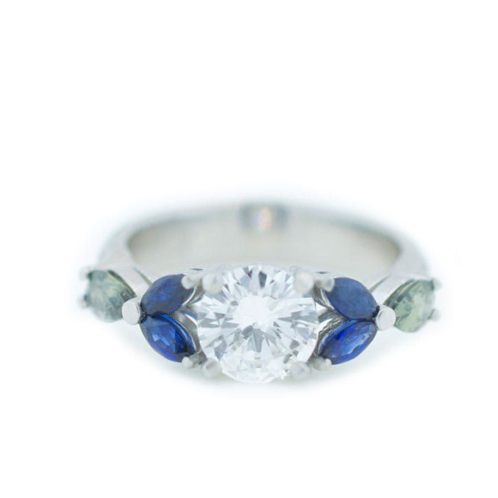 Custom engagement ring made with platinum, 1 carat diamond; 0.49 ctw blue sapphires, 0.50 ctw green sapphires, and 0.08 ctw diamond melee custom made and designed by Abby Sparks Jewelry, The Janet.